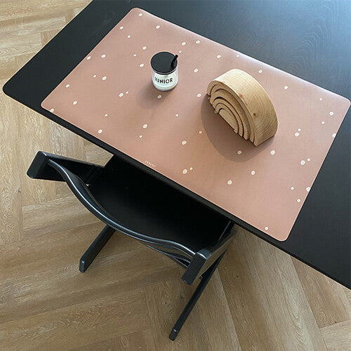 Een eeveve bureaumat met stippen op een zwarte tafel met een houten regenboog en kaars.