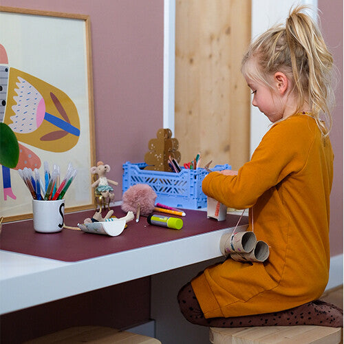 Meisje aan een bureau met een rode eeveve bureaumat en knutselspullen.