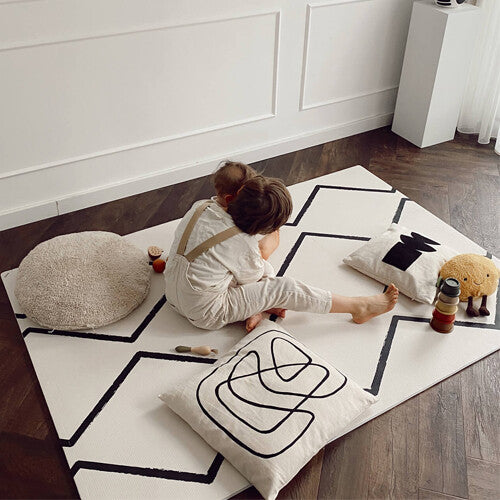 Twee kinderen zitten en spelen op de eeveve foam speelmat met zwart geometrisch patroon.