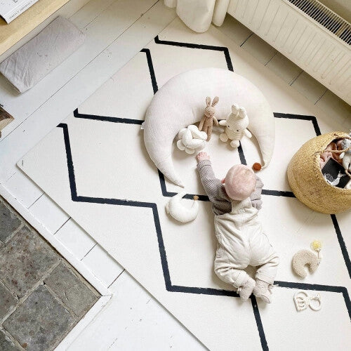 Een baby ligt op de buik op de eeveve foam speelmat met zwart geometrisch patroon en speelt met rammelaars.