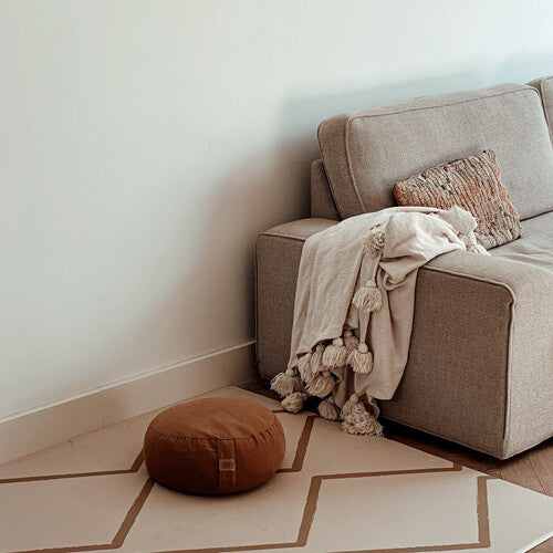 eeveve foam speelmat met beige geometrisch patroon op de vloer naast een bank met een poef.
