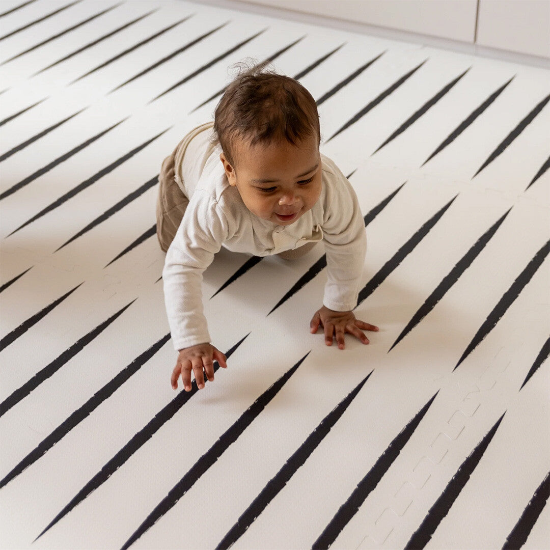 Een baby kruipt op de eeveve foam speelmat met ecru en zwart geometrisch patroon.