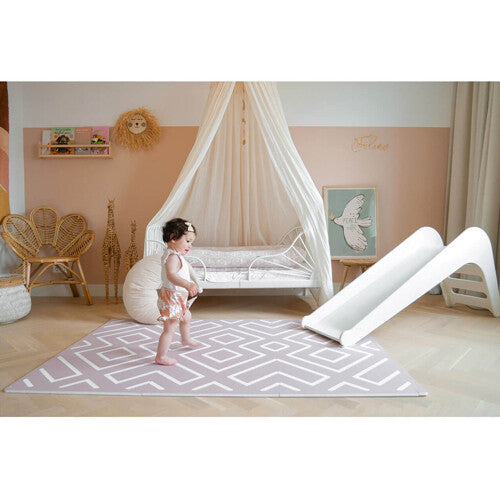 Een baby staat op de eeveve foam speelmat in oud roze met geometrisch patroon in een kinderkamer.