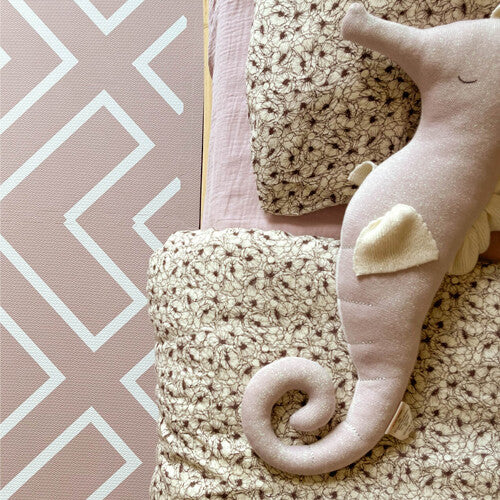 Detail van de eeveve foam speelmat naast een bed met een bloemendekbed en een roze zeepaard knuffel.