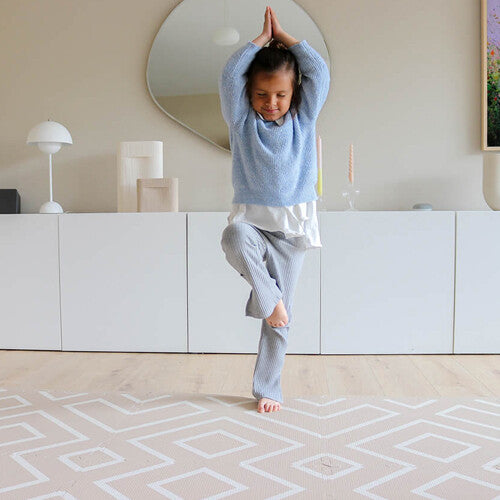 Een kind doet een yoga-oefening op de eeveve foam speelmat met beige en wit geometrisch patroon.