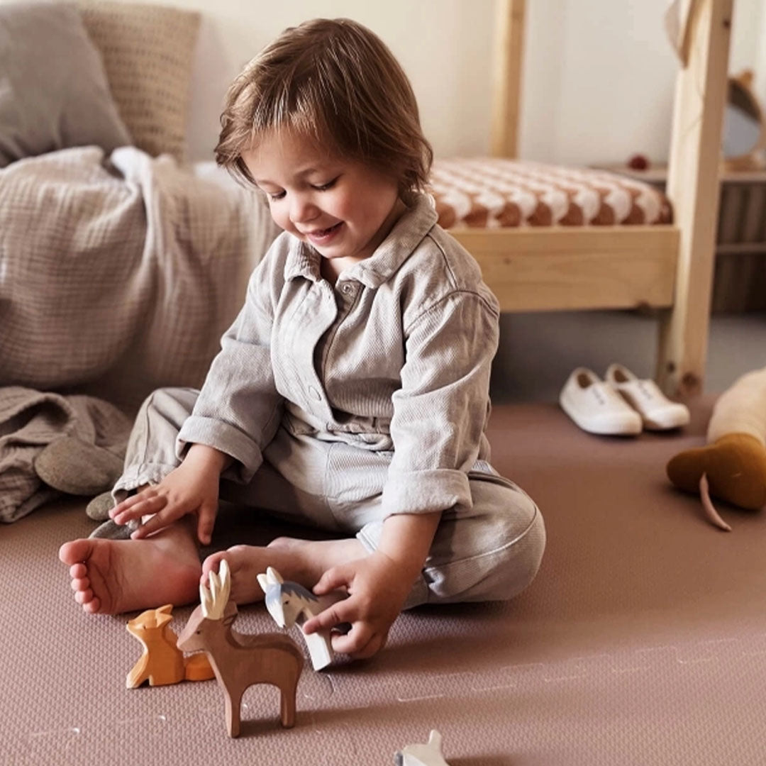 Een lachend kind speelt op de eeveve foam speelmat met houten dierenfiguren.