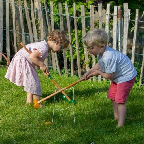 Twee kinderen spelen croquet met een Egmont Toys croquet set in een groene tuin.