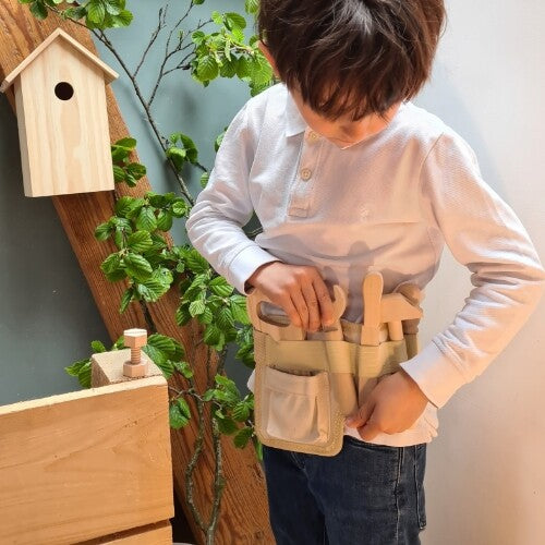 Een kind draagt de Egmont Toys beige gereedschapsgordel met houten speelgoedgereedschap.