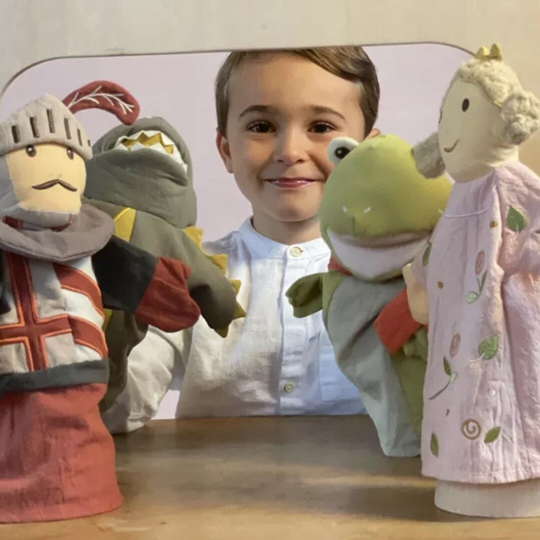 Een jongen speelt met verschillende handpoppen, waaronder een draak, een kikker, een ridder en een prinses, in een poppentheater.