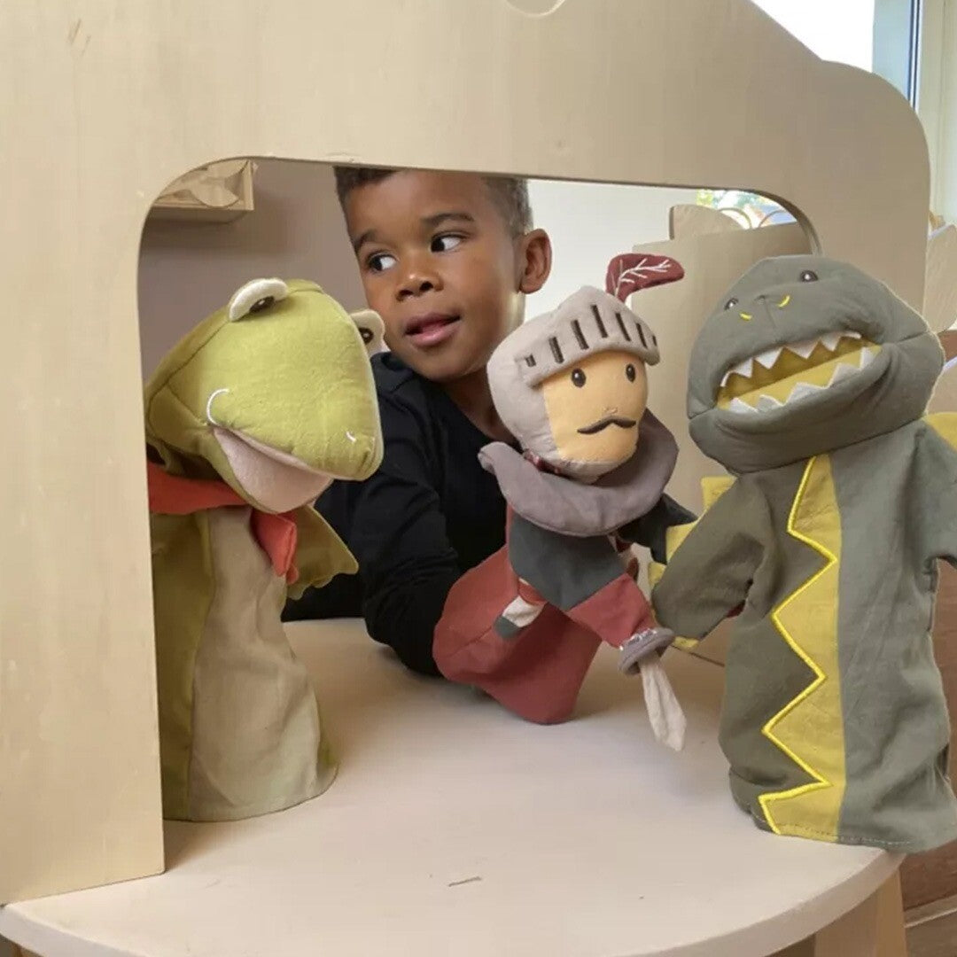 Kind speelt met drie handpoppen, waaronder een kikker, in een houten poppenkast.