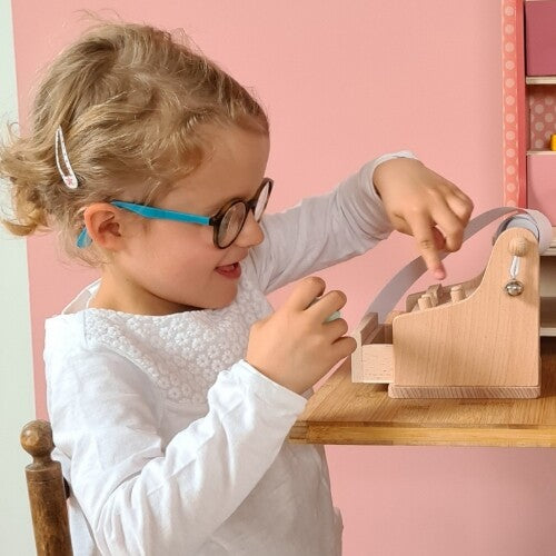 Een meisje met bril speelt met de houten kassa op een tafel.