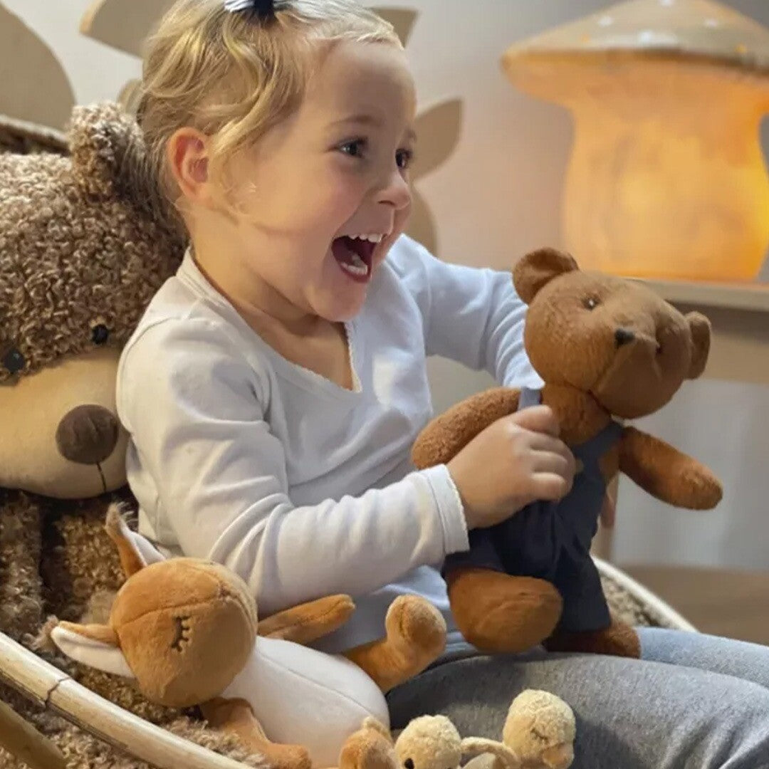 Een lachend kind speelt met de bruine knuffelbeer Gabin en andere pluchen speelgoedbeesten.