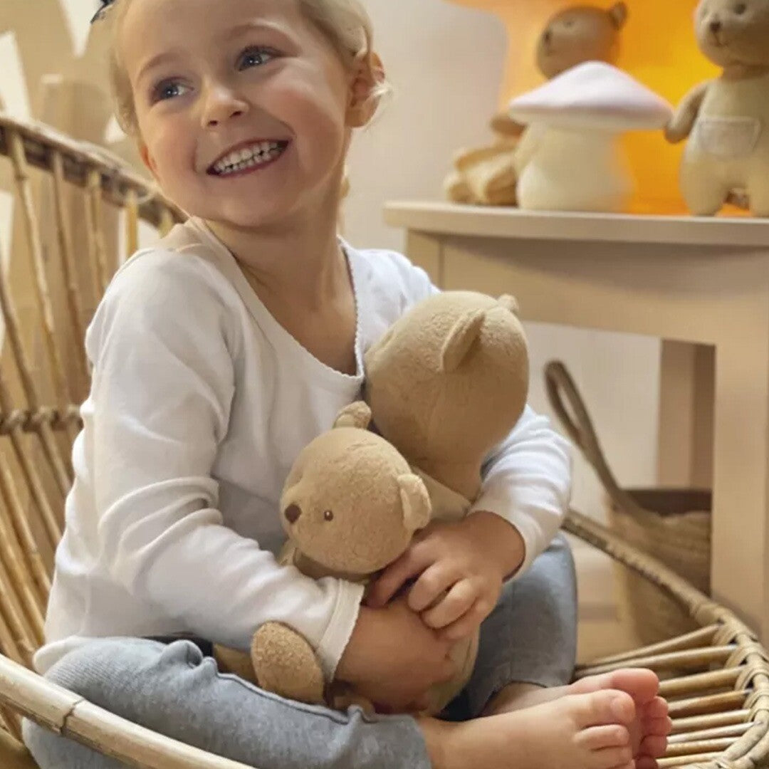 Een lachend meisje knuffelt de beige pluchen beer Marcel.