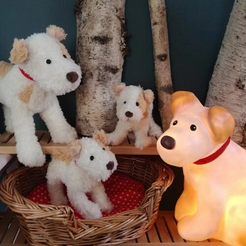 Een collectie Egmont Toys knuffelhonden en een hondenlamp op een plank, met berkenstammen op de achtergrond.