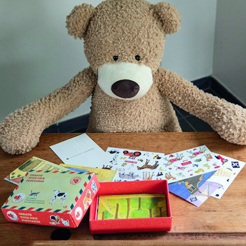 Een teddybeer zit aan een houten tafel met de Egmont Toys knutselset postkaarten met stickers, inclusief open doos, stickervellen en versierde kaarten.