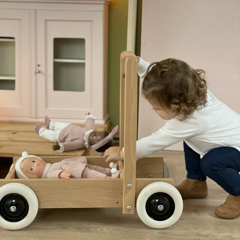 Een kind speelt met de houten loopwagen waarin twee poppen liggen.