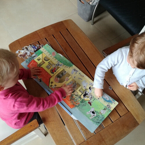 Twee kinderen spelen met het Egmont Toys magneetboek boerderij op een houten tafel.