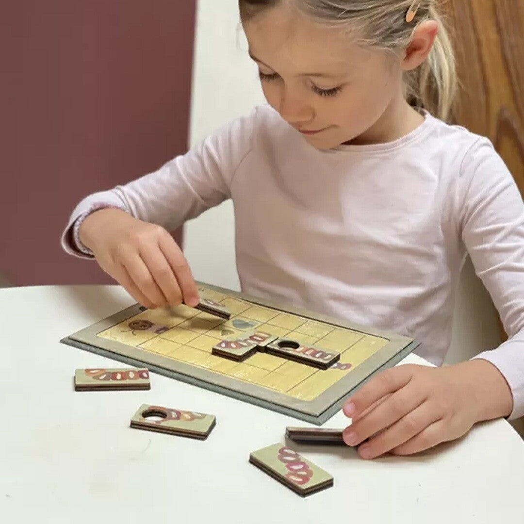 Een meisje speelt geconcentreerd met het magnetische rupsenspel aan tafel.