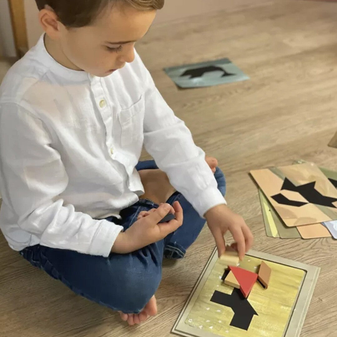 Een jongen zit op de grond en legt een stukje van het tangram spel op een puzzelkaart.
