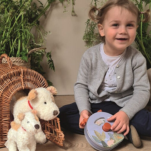 Lachend kind zit op de grond en speelt met de Egmont Toys muziekdoos, naast een mand met knuffelhonden.