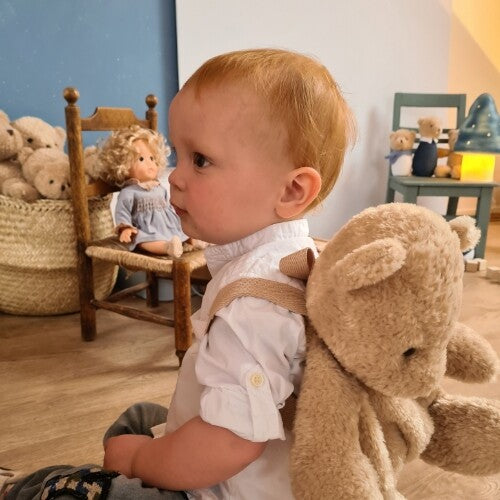 Een peuter met rood haar draagt de beige teddybeer peuterrugzak op de rug.