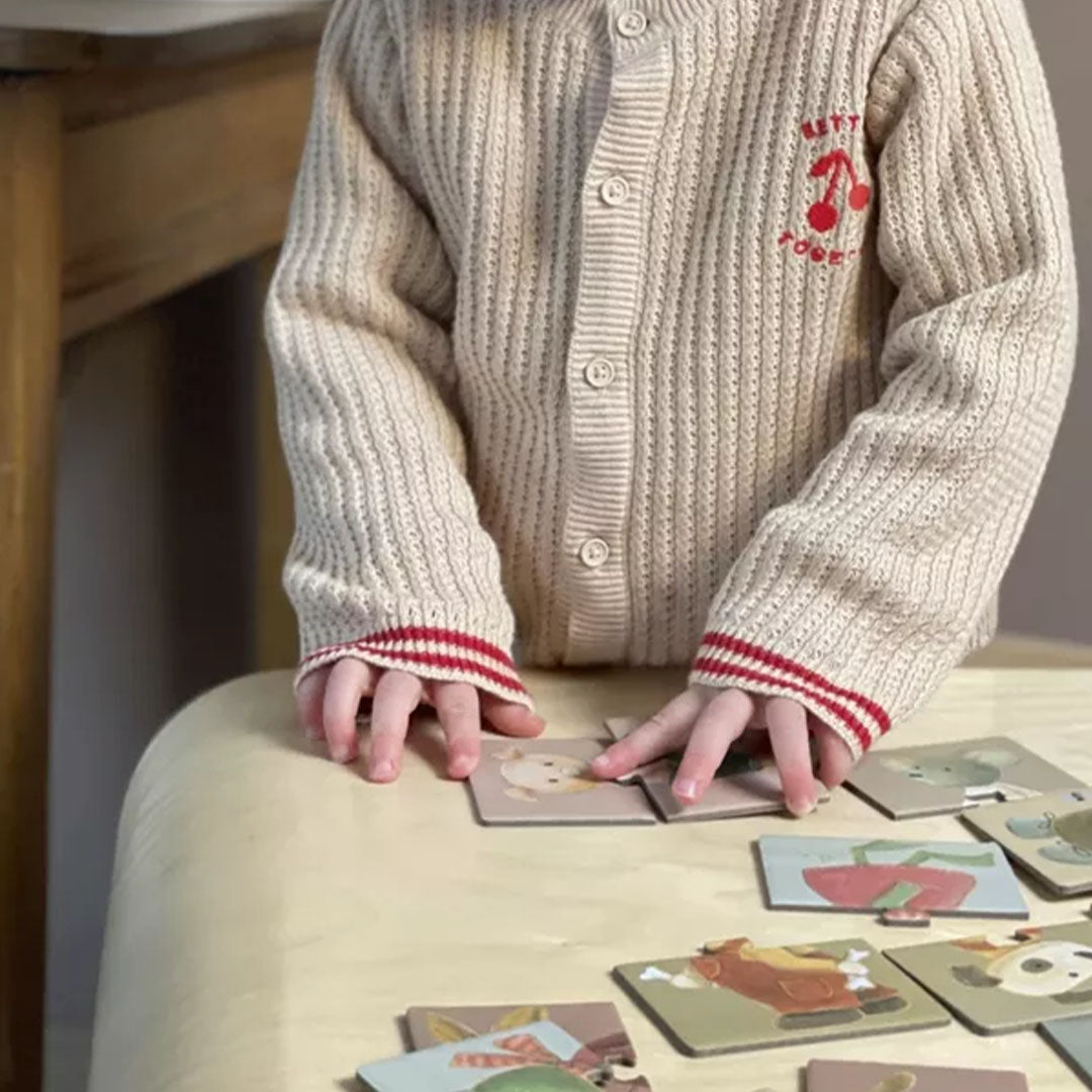 Een kind met een beige vestje legt de Egmont Toys mix en match dierenpuzzelstukjes op een tafel.