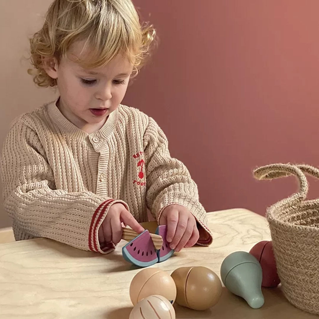Een kind snijdt een houten speelgoed watermeloen met een houten mes.