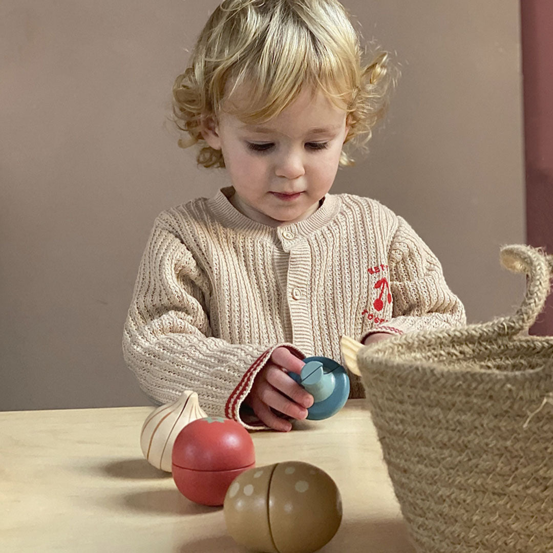 Een kind houdt een blauw houten speelgoed vast en een houten mes.