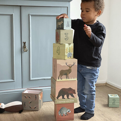 Een kind speelt met Egmont Toys stapelblokken met bosdieren, staand naast een hoge toren.