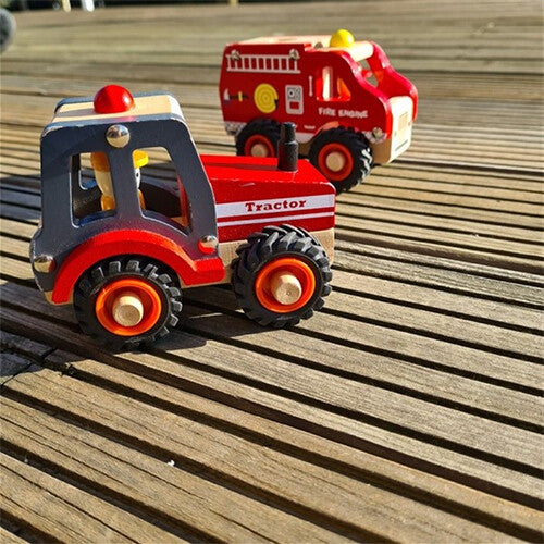 Een rode houten speelgoedtractor staat op een houten vlonder, met een houten brandweerwagen op de achtergrond.