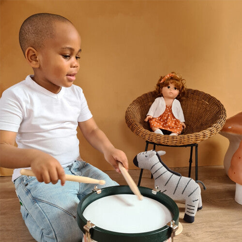 Een kind speelt op de Egmont Toys trommel met diamantpatroon, met een pop en zebra op de achtergrond.