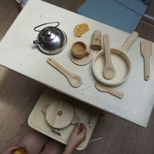 Bovenaanzicht van een kind dat speelt met de Egmont Toys zilveren waterketel en houten speelgoedkeukengerei op een tafel.