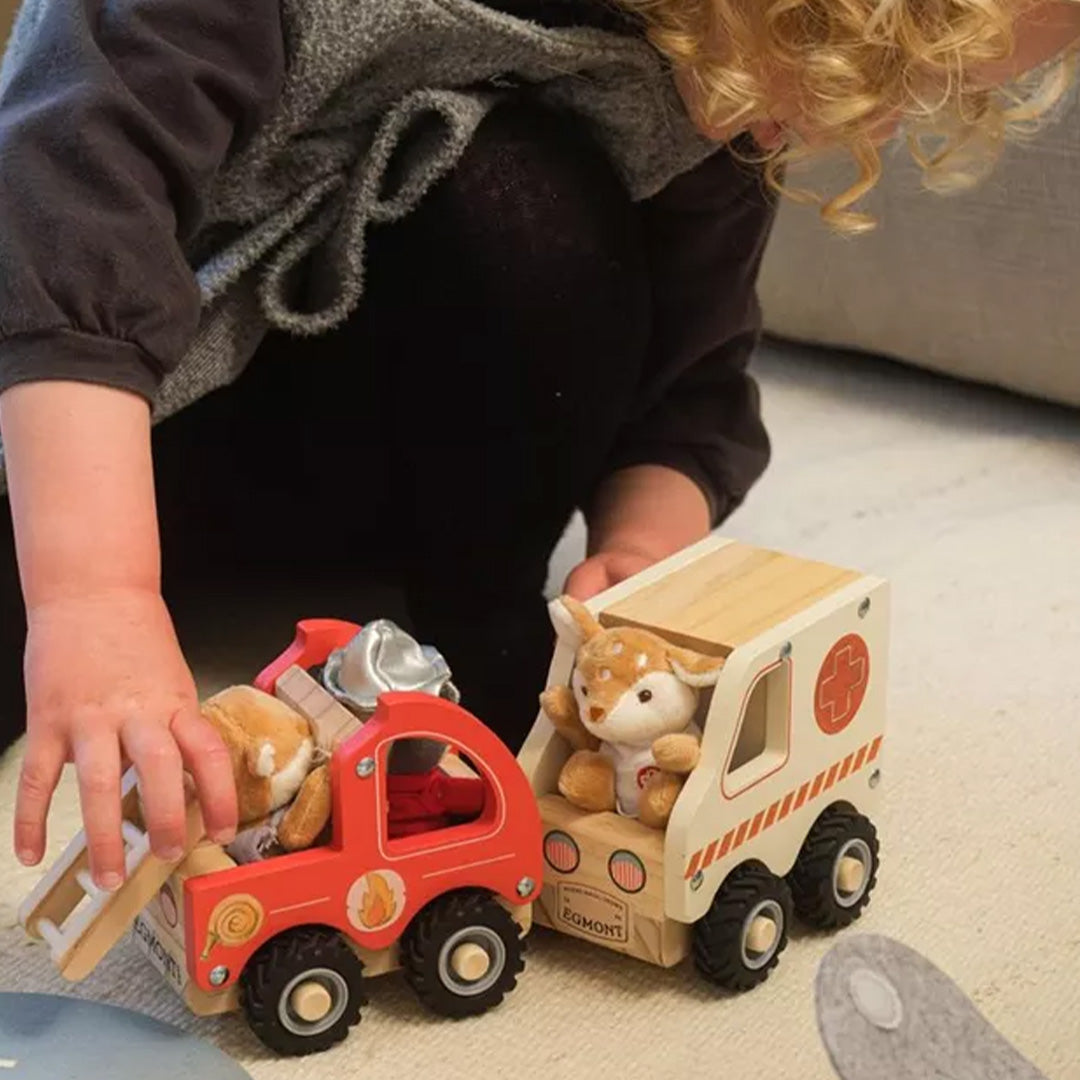 Een kind speelt met de Egmont Toys houten ambulance met knuffelhert en een rode houten brandweerwagen.