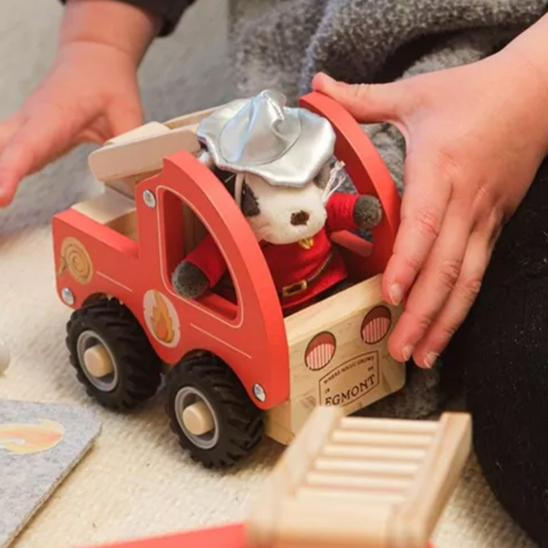 Kinderhanden spelen met de Egmont Toys houten brandweerwagen waarin de knuffeldas zit.
