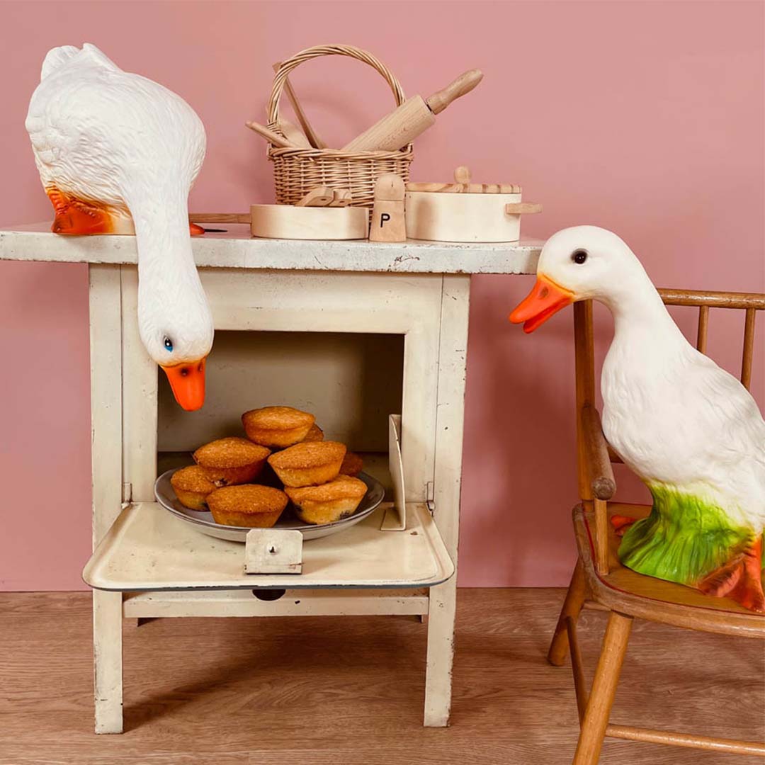 Egmont Toys Heico eendenlamp kijkt naar cupcakes in een speelgoedoventje, naast een andere eend op een stoel.