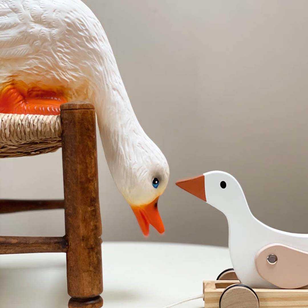 Egmont Toys Heico eendenlamp kijkt naar een houten trek-eendje op een witte tafel.