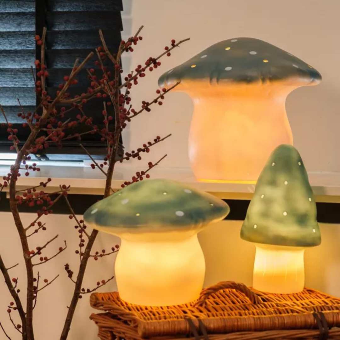 Drie gloeiende Egmont Toys vliegenzwam nachtlampen van verschillende formaten staan op een rieten mand.