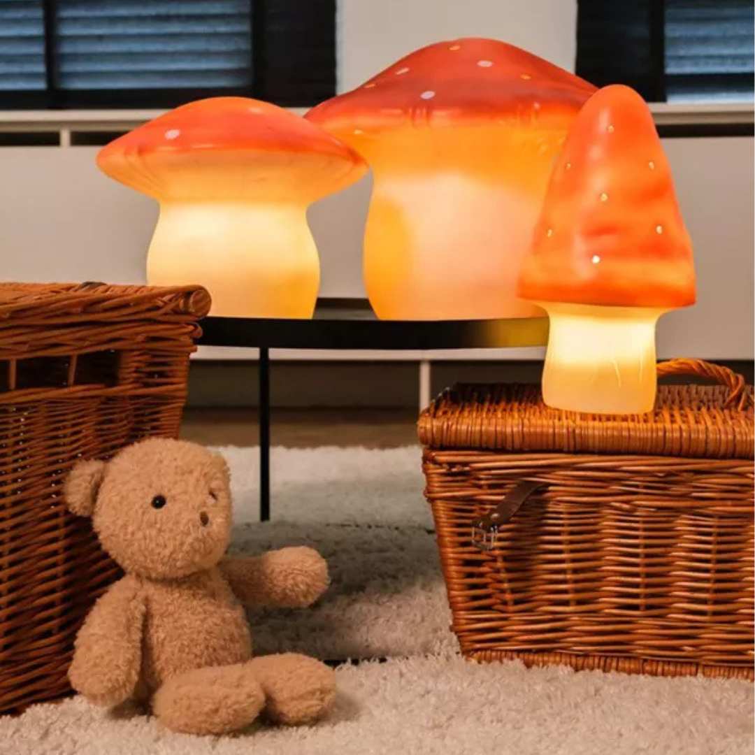 Drie brandende Egmont Toys vliegenzwam nachtlampen van verschillende formaten in een kinderkamer met een teddybeer.
