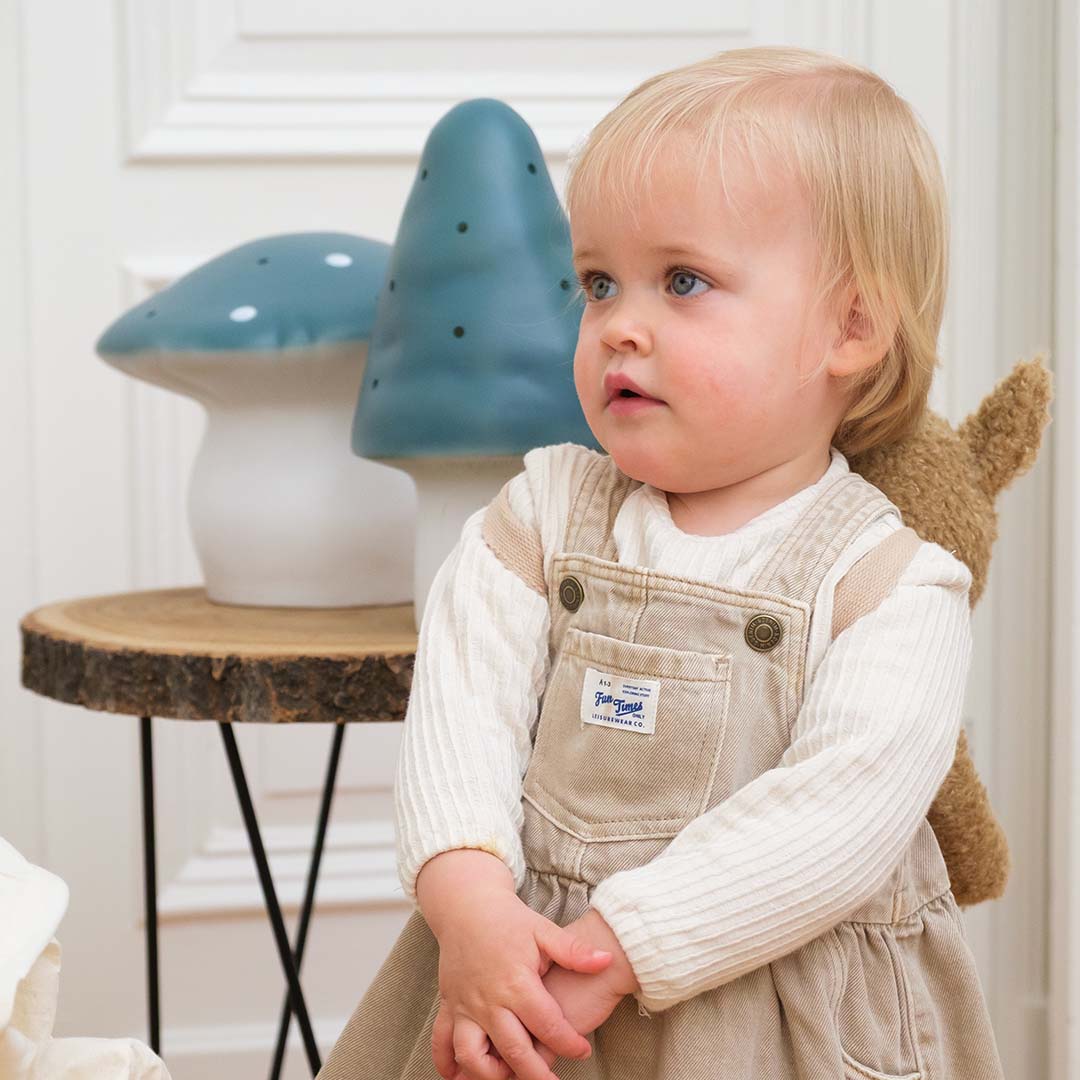 Een peuter zit voor twee Egmont Toys paddenstoel nachtlampen die op een houten bijzettafel staan.