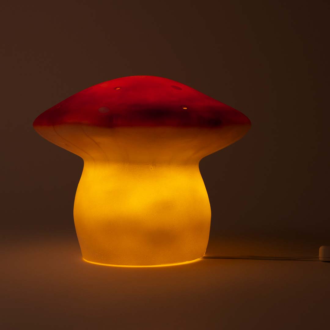 Een rode vliegenzwam nachtlamp met witte stippen die warm geel licht geeft in het donker.