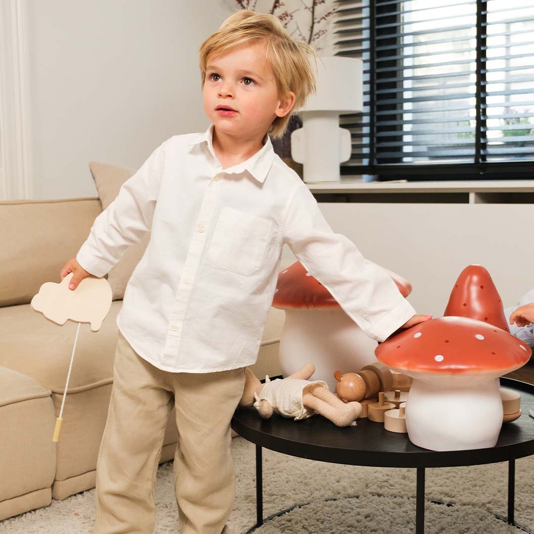 Een jongen staat naast een salontafel met twee Egmont Toys vliegenzwam nachtlampen en ander speelgoed.