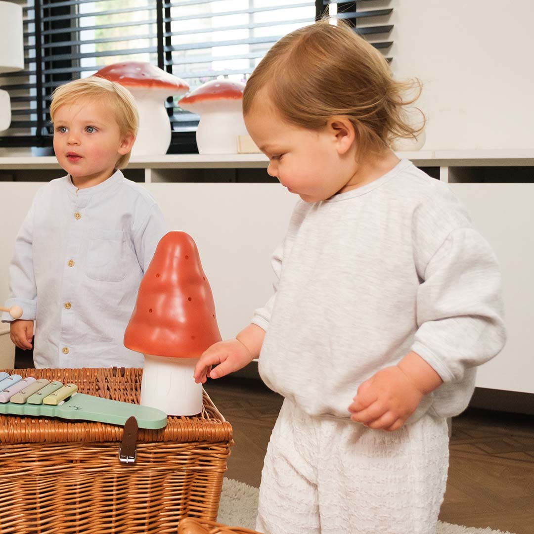 Twee kinderen spelen in een kamer met een Egmont Toys paddenstoel nachtlamp op een rieten mand.