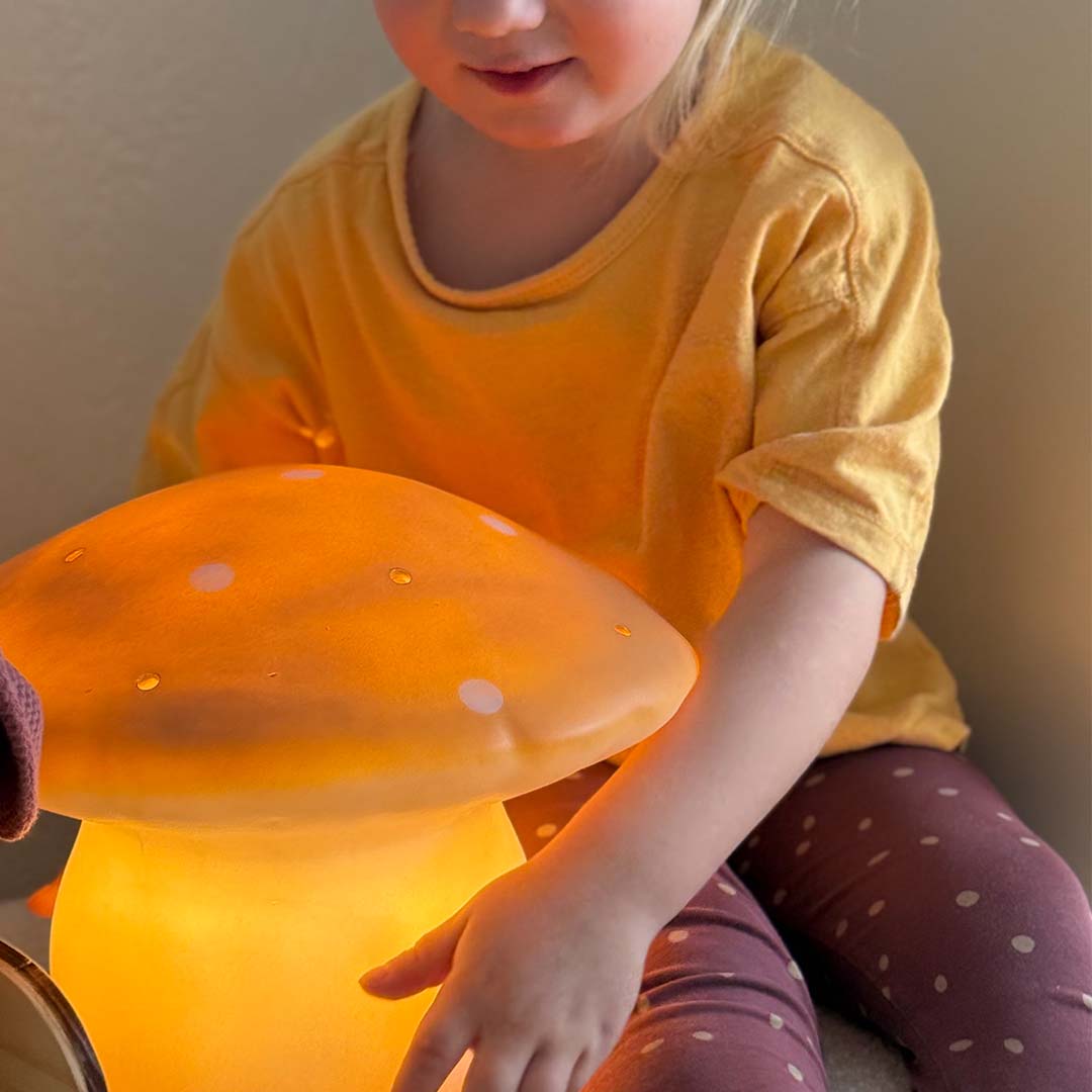 Een kind raakt de gloeiende Egmont Toys vliegenzwam nachtlamp aan.