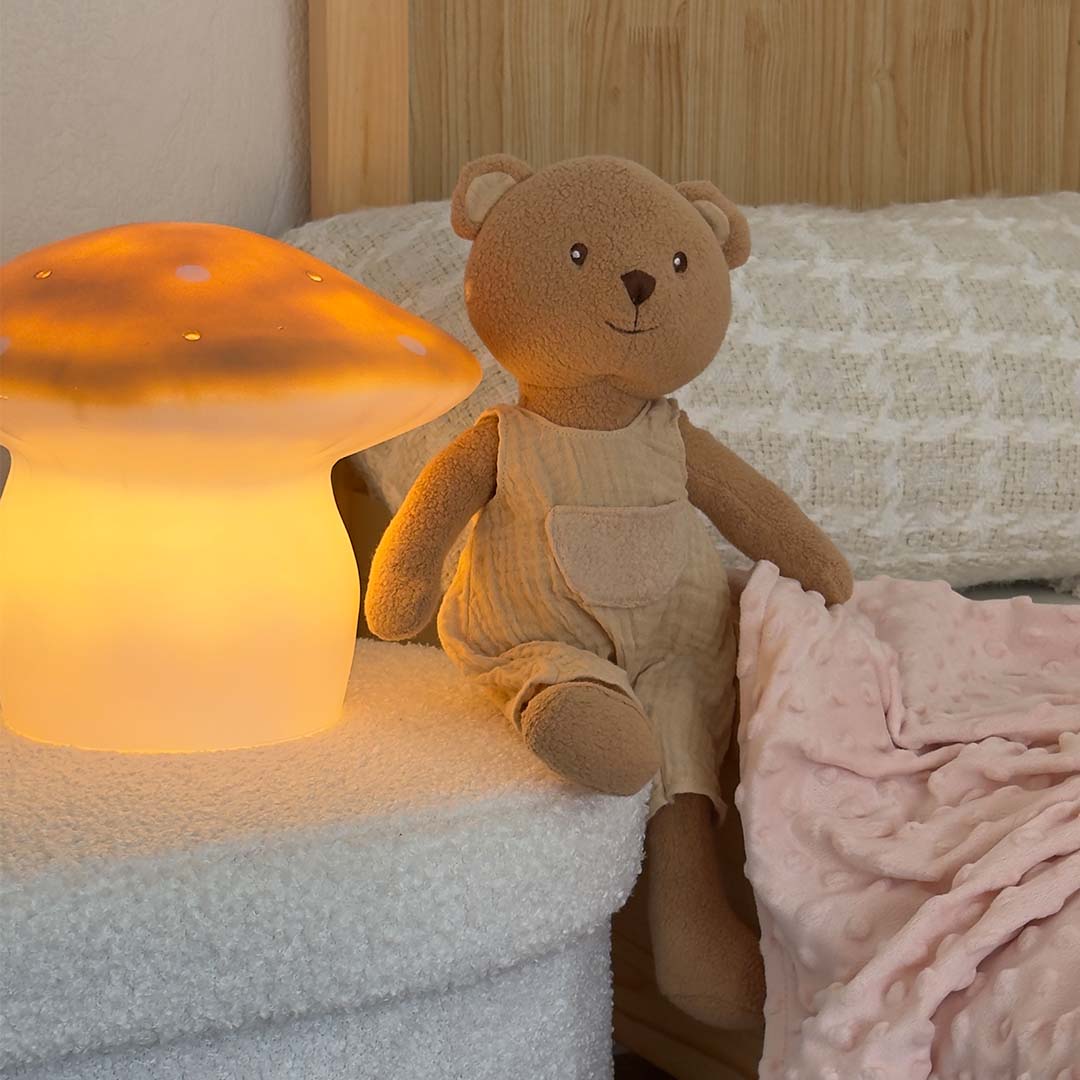 De Egmont Toys vliegenzwam nachtlamp brandt naast een teddybeer op een bed.