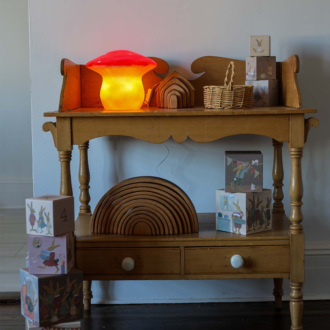 De Egmont Toys vliegenzwam nachtlamp brandt op een houten tafel tussen houten speelgoed.