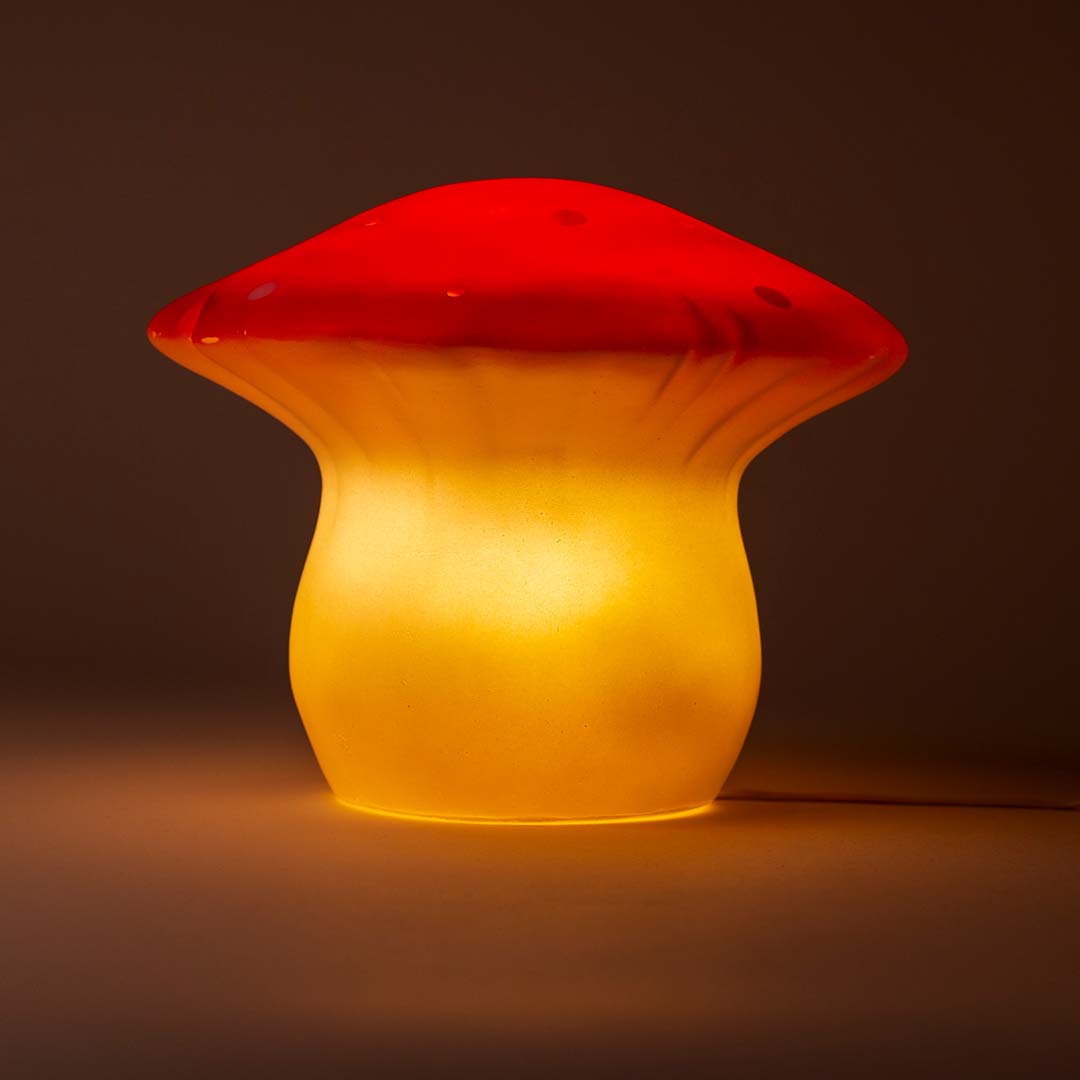 De Egmont Toys vliegenzwam nachtlamp brandt en geeft een warm geel licht in een donkere omgeving.