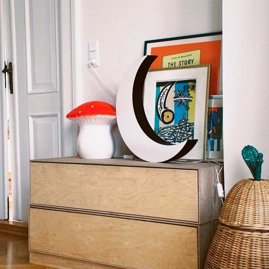 De Egmont Toys vliegenzwam nachtlamp staat op een houten ladekast naast een maanlamp en ingelijste kunst.