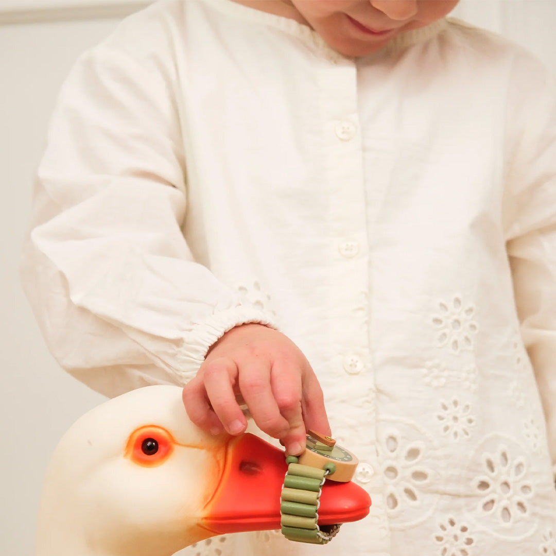 Een kind speelt met het Egmont Toys houten horloge en een witte ganzenknuffel.