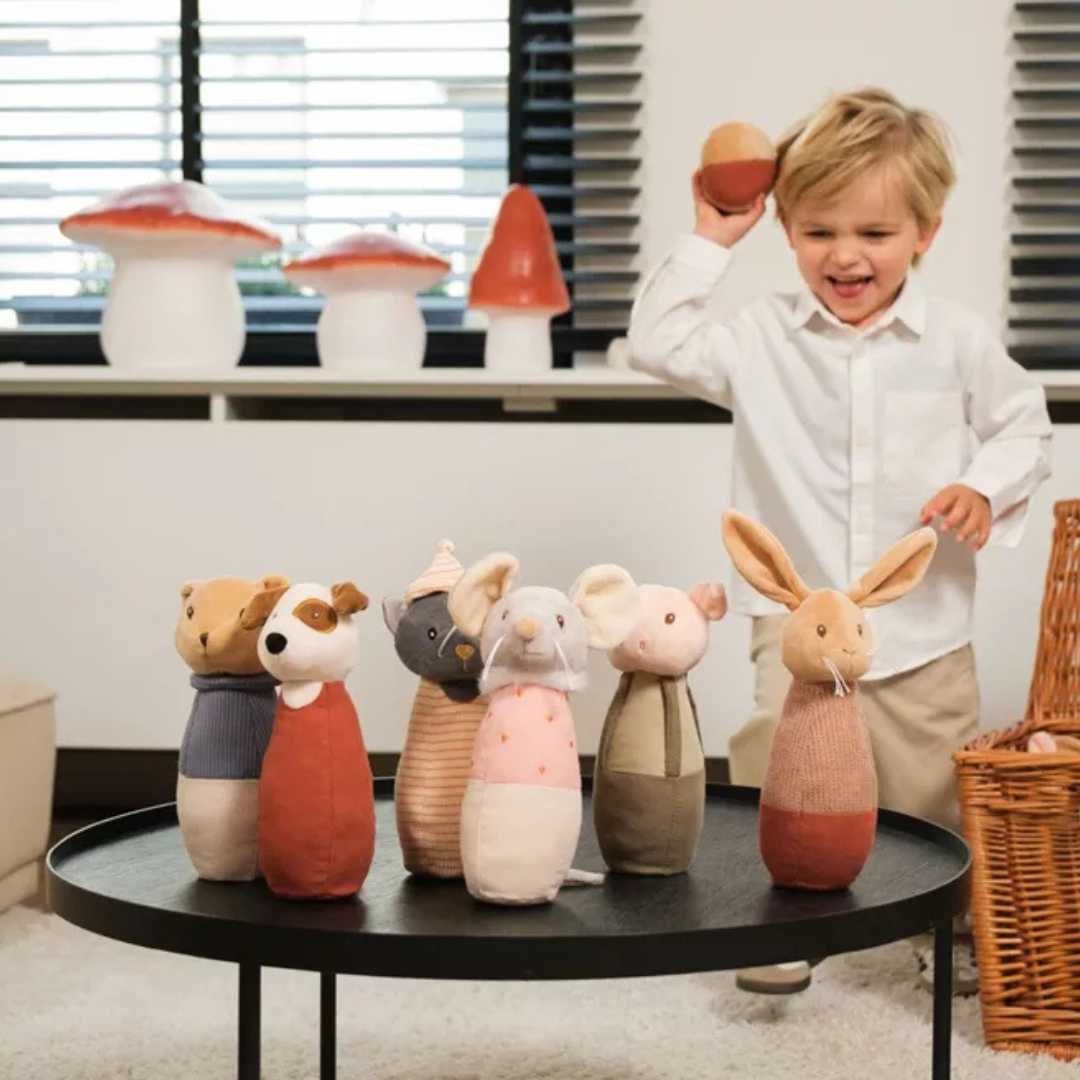 Een lachende peuter speelt met het Egmont Toys stoffen dieren kegelspel op een zwarte tafel.