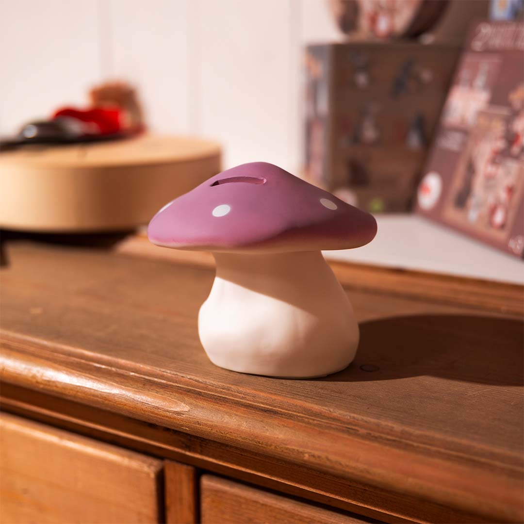 Lila paddenstoel spaarpot met witte stippen op een houten dressoir.